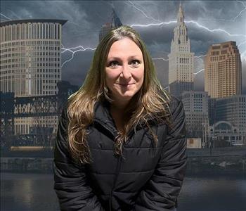 Picture of a blonde woman in a black winter coat in front of a stormy Cleveland background